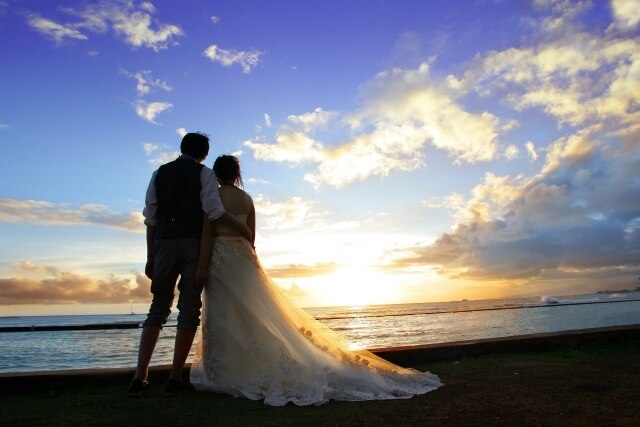 夕陽を前に海辺に佇む新郎新婦