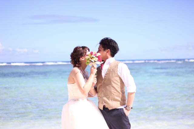 ブーケの向こうでキスをする新郎新婦。背景は青い海。
