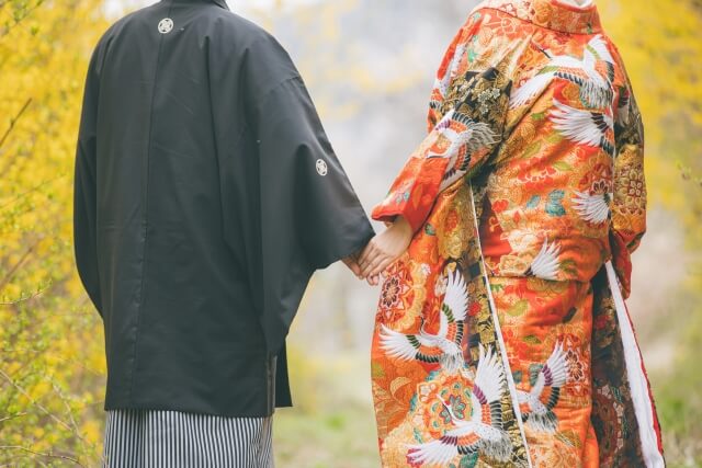 紅葉を前に佇む紋付袴姿の新郎と色打掛を着た新婦