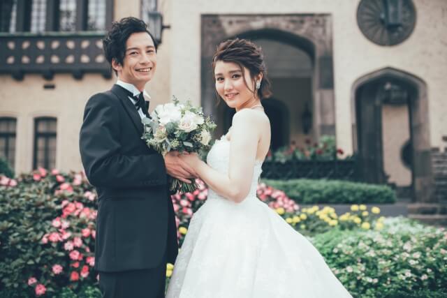 庭園をバックに微笑むタキシード姿の新郎とウエディングドレス姿の新婦